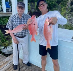 two senior men in hat hold up red snapper fish
